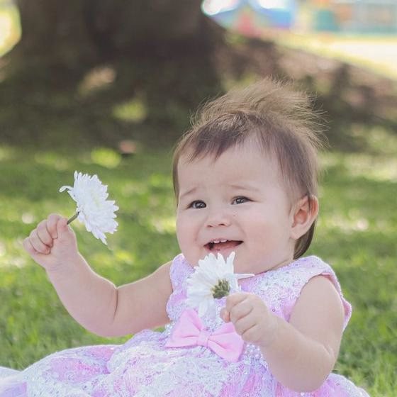 Retrato de la bebé sonriendo con una flor blanca en la mano
